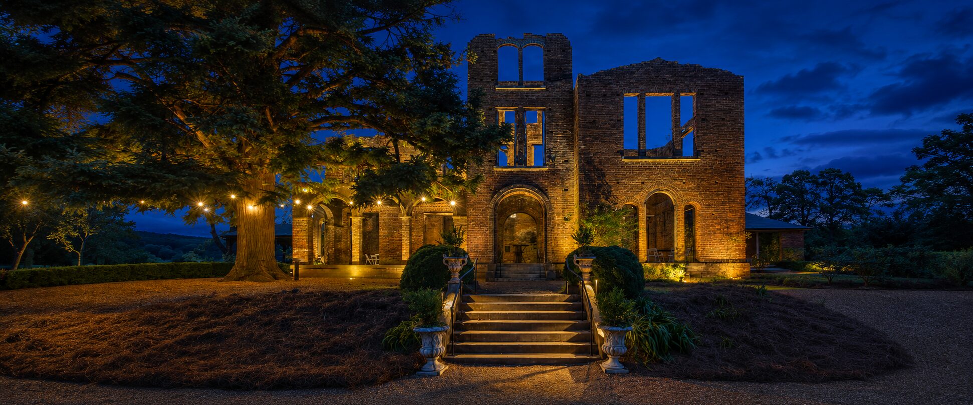 Historic brick building and entrance steps at Barnsley Gardens illuminated with warm exterior lighting by Georgia Lightscapes.